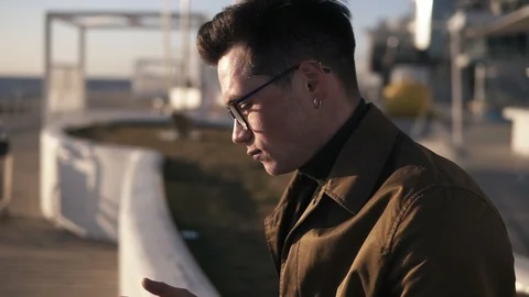 Side view of a elegant nab in glasses and brown coat sitting outside on parapet Video stock 108649992
