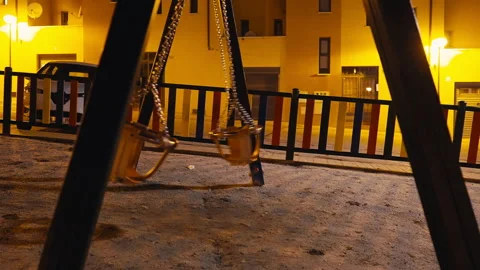 Side view empty baby swings swinging in yellow street light at night in city. No Stock Footage 247120681
