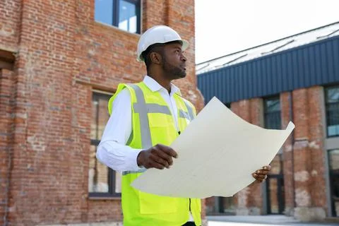 Side view of the engineer wearing white helmet and holding building project in Stock Photos