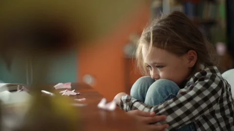 Side view of exhausted upset primary child school girl sitting alone hugging Video stock 159651410