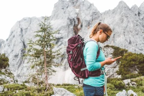 Side view of female backpacker looking at her phone, mountains in the background Stock Photos