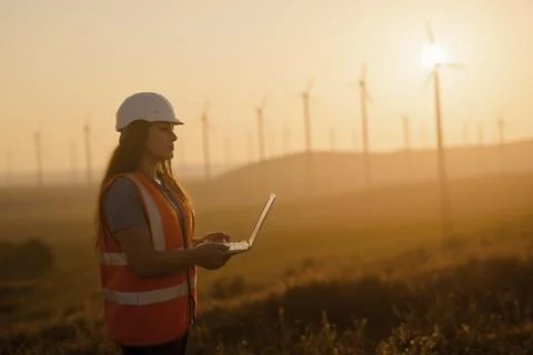 Side view of a female engineer in a hard hat and orange safety vest using a l Stock Photos