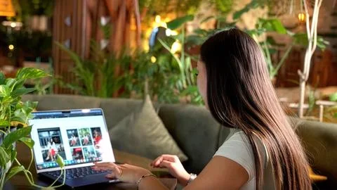 Side view of female freelancer using laptop in green cafe for remote work Stock Photos