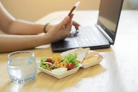 Side view of a female hands working on a wooden desk with healthy food near.. Stock Photos