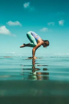 Side view of female practicing yoga on stone in water Stock Photos