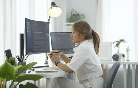 Side view female programmer analyzing data code on multiple monitor screens.. Stock Photos