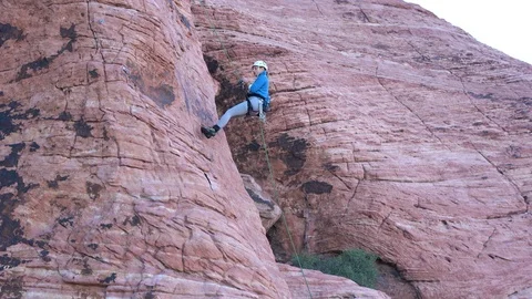 Side view of female rock climber rappelling, abseiling down a sandstone wall Stock Footage 122903395