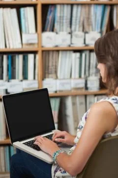 Side view of a female student against bookshelf using laptop in library Stock Photos