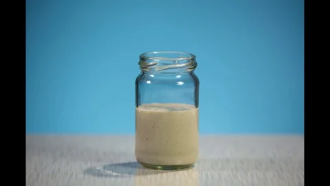 Side view of the fermentation process of wheat dough in a jar on a blue backgrou Stock Footage 129884001
