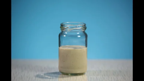 Side view of the fermentation process of wheat dough in a jar on a blu7 4 Stock Footage 129884039