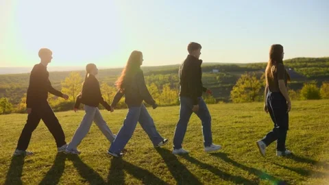 Side view of five students walking in a sequence on a green hill Stock Footage 334560335