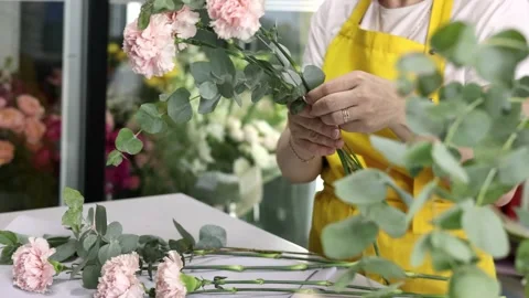 Side view of a flower shop assistant in yellow apron tying a bunch of flowers 動画素材 160950938