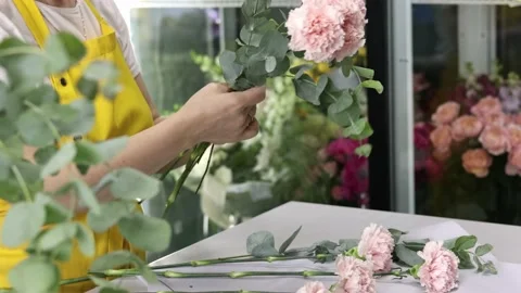 Side view of a flower shop assistant in yellow apron tying a bunch of flowers Video stock 161377674