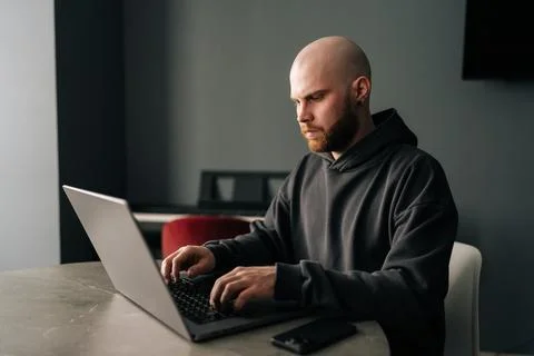 Side view of focused male programmer with beard and hoodie diligently typing on 스톡 사진