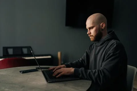 Side view of focused male programmer wearing dark hoodie typing code on laptop Stock Photos