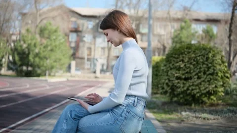 Side view of a focused young student sitting on a park bench, browsing and Stock Footage 347220180