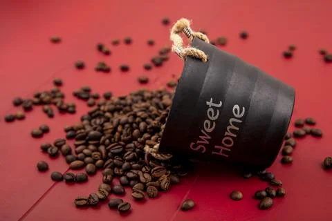 Side view of fresh coffee beans falling out of black basket on red background Stock Photos