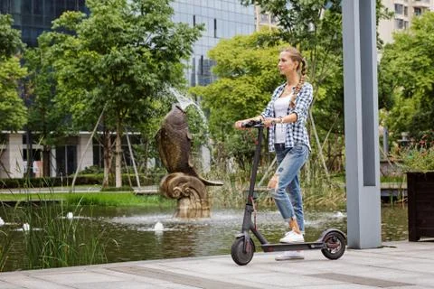 Side view full length of modern stylish young woman riding on electric scooter 스톡 사진