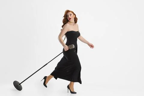 Side view full-length portrait of female singer carrying microphone and running Stock Photos