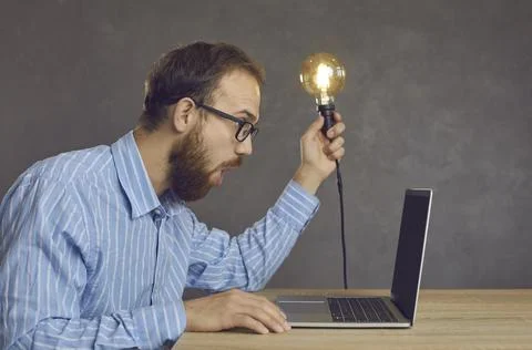 Side view of a funny surprised man sitting in front of a laptop with a light Stock Photos