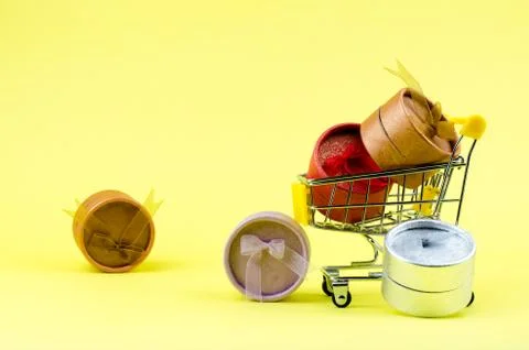 Side view of a gift box in and near a shopping cart on a yellow background Stock Photos