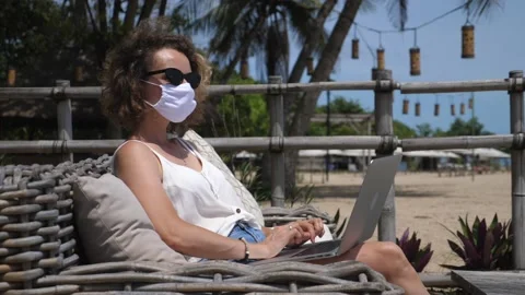 Side view of a girl in protective face mask working on a laptop on the beach Stock Footage 146363662