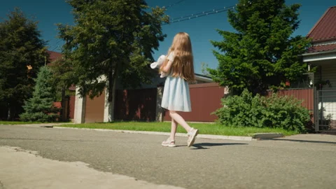 Side view of girl walking with stuffed rabbit on empty suburban street Vídeo Stock 310213855