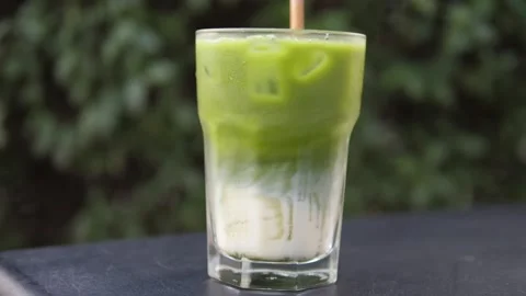 Side view of glass with matcha tea and soya milk layers mixed together. Cold Stock Footage 144901700