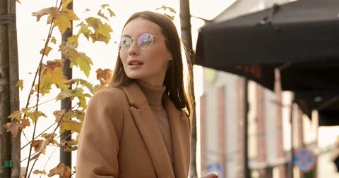 Side view of gorgeous young lady in eyewear and beige coat standing on street Stock Footage 142544611