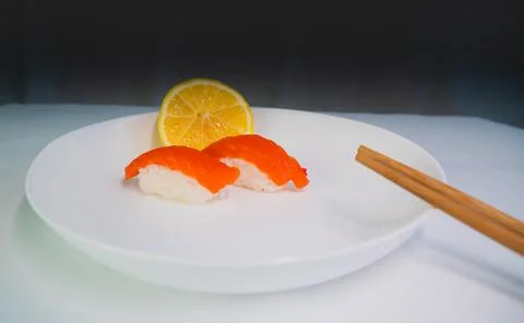 Side view, on a gray and white background, a white plate with sushi and lemon Stock Photos