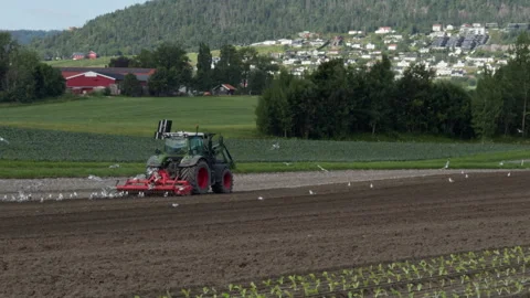 Side view of green tractor with red rotary tiller preparing soil for planting Stock Footage 341319444