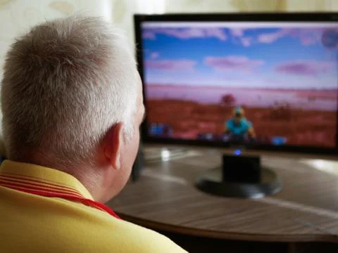 The side-view of a grey haired senior man sitting at the table and playing a  Stock Photos