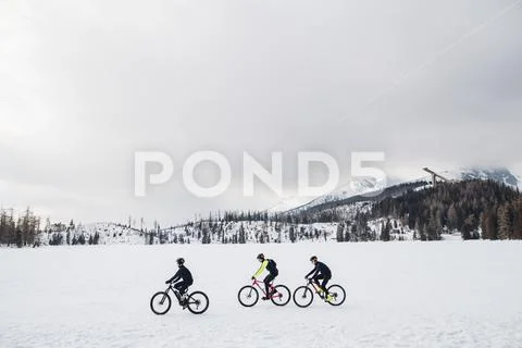 Side view of group of mountain bikers riding outdoors in winter. Stock Photos