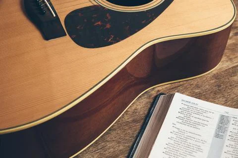 Side view of a guitar and a bible on a wooden background in a dimly lit envir Stock Photos