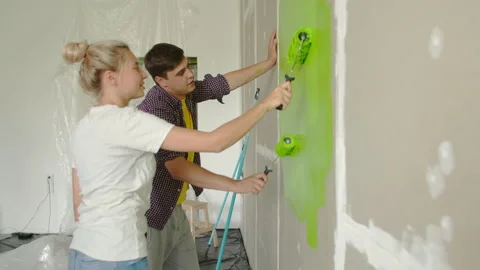 Side view of a guy and a girl painting the wall green. A young girl and a guy Stock Footage 205044255