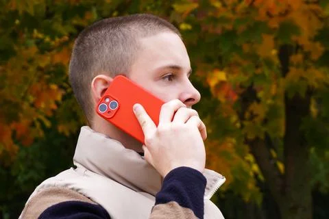 Side view, guy with a red smartphone in an autumn park. young handsome man is Stock Photos