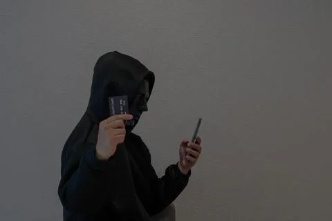 Side view Hacker, masked individuals holding phone and credit cards Foto stock