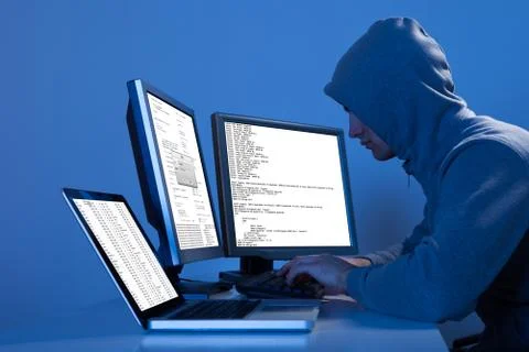 Side view of hacker using multiple computers to steal data at table Stock Photos