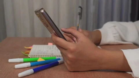Side view of hand holding phone while writing on book on wooden table Stock Footage 277013544