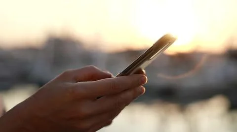 Side view of the hand of a woman using a smartphone on the beach at sunset or Stock Photos