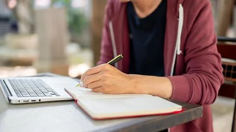 Side view of hand writing in notebook with ballpoint pen while sitting in f.. Stock Photos