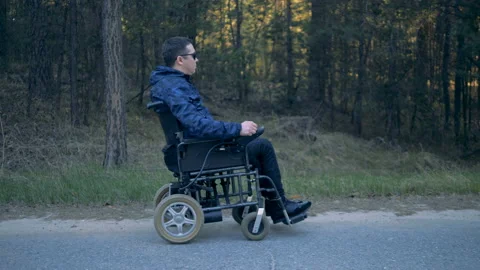 Side view of a handicapped man moving along the road in his powered wheelchair Stock Footage 90918849