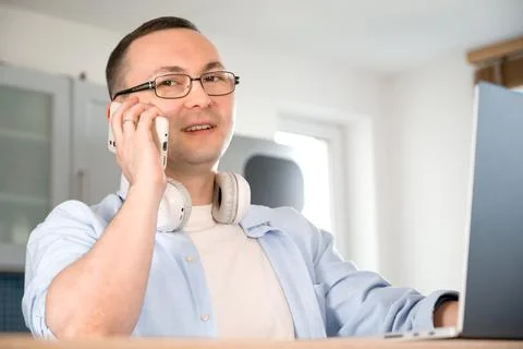 Side view on happy asian man talking on the phone and looking at laptop scree Stock Photos