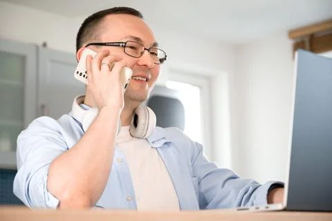 Side view on happy asian man talking on the phone and looking at laptop scree Stock Photos