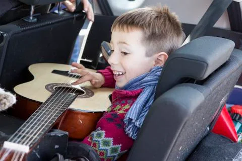 Side view of happy boy playing guitar in car Stock Photos