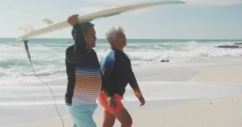 Side view of happy senior hispanic couple walking on beach with surfboard Stock Footage 341930949