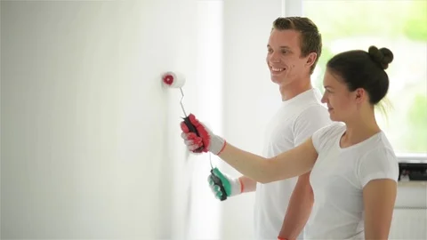 Side View of Happy Smiling Couple Painting the Wall with White Paint in Their Stock Footage 80968460