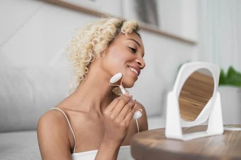 Side view on happy smiling dark skinned girl massagin face with jade roller Stock Photos