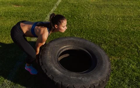 Side view image of athlete strong fitness woman doing tire-flip outdoors on g Stock Photos