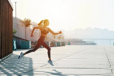 Side view image of a brunette running on the pavement outdoors. Low angle Stock Photos